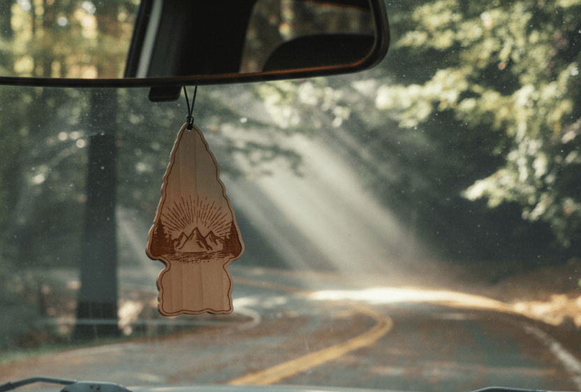 Car air freshener hanging from a car's rearview mirror with a scenic road in the background
